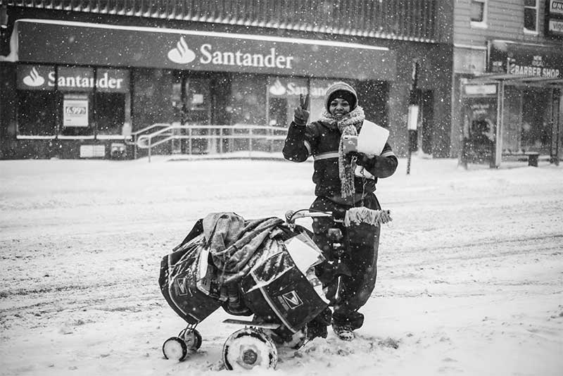 Mail carrier delivering mail in the snow giving a peace sign